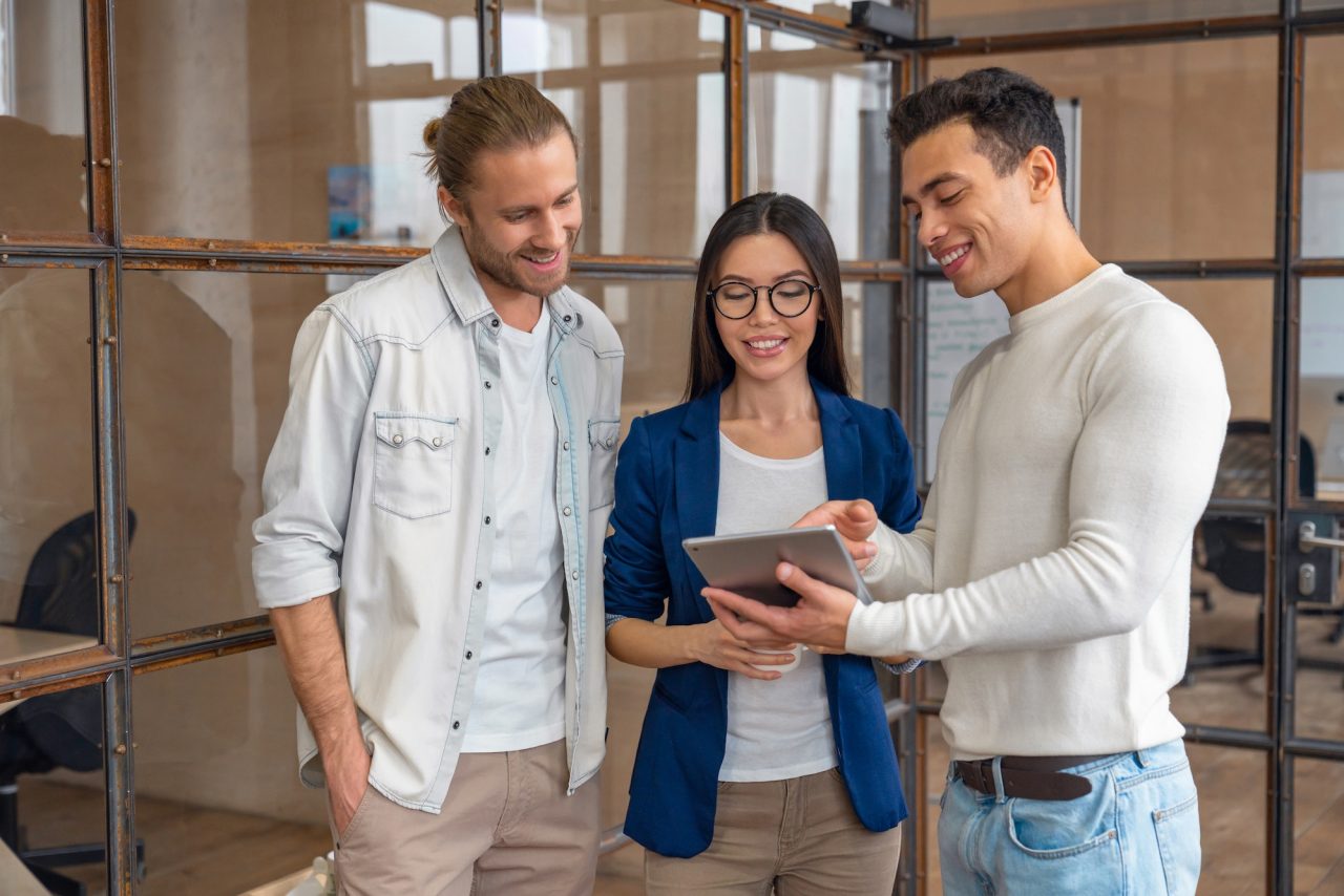 three young business professionals standing together and discussing over business report New Era Digital